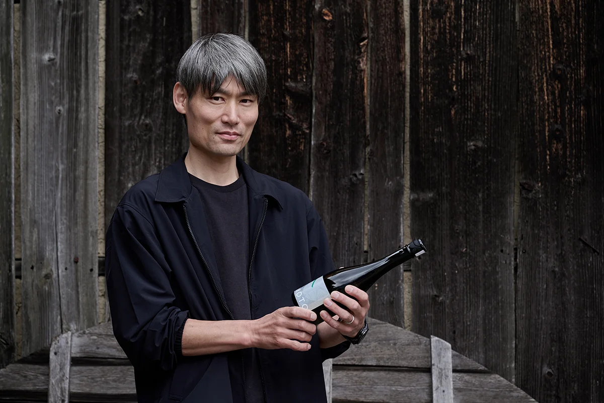 倉本酒造の蔵の前で倉本隆司さん。手に持つのは「KURAMOTO SE」